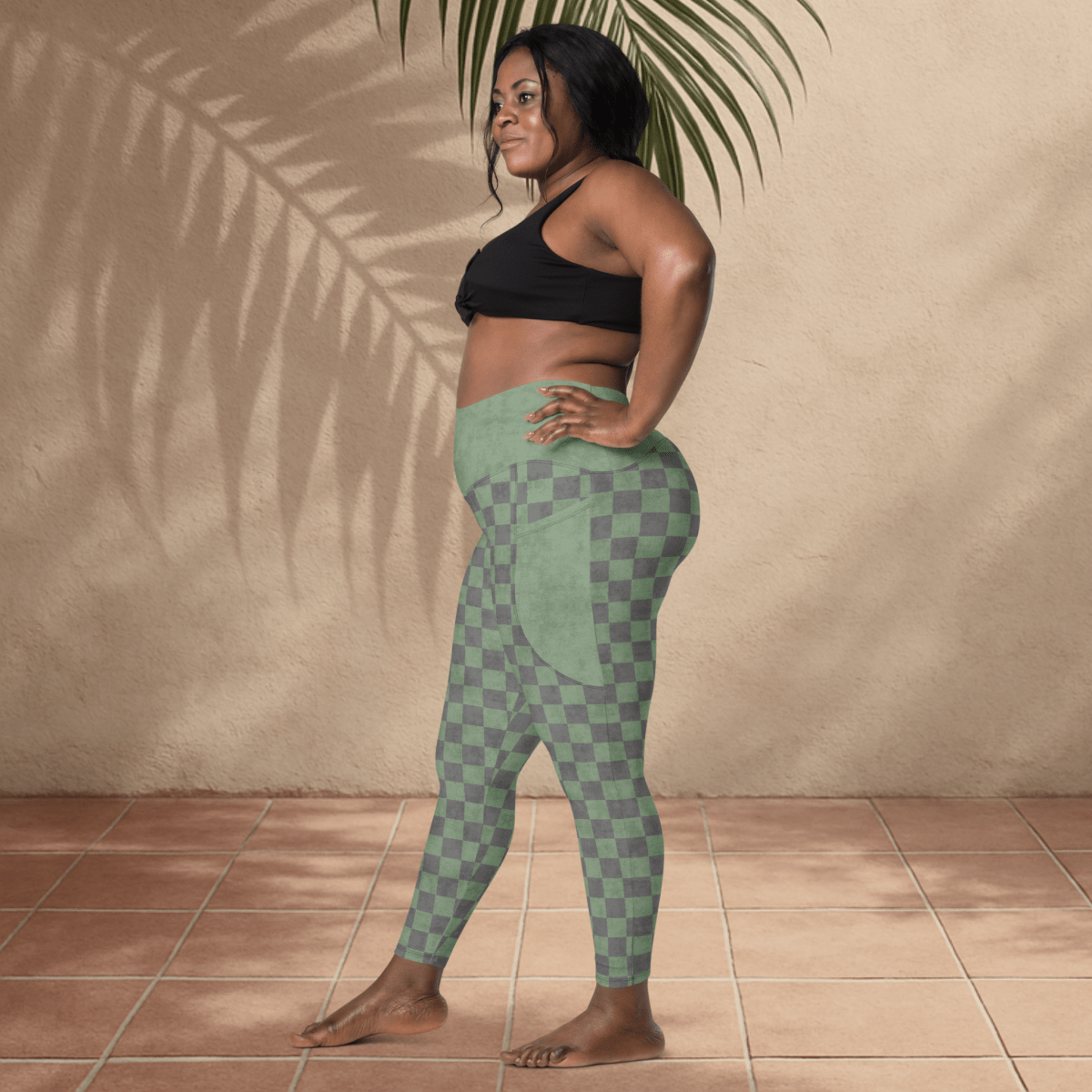 Woman wearing green checkered leggings and black sports bra standing against a beige wall.