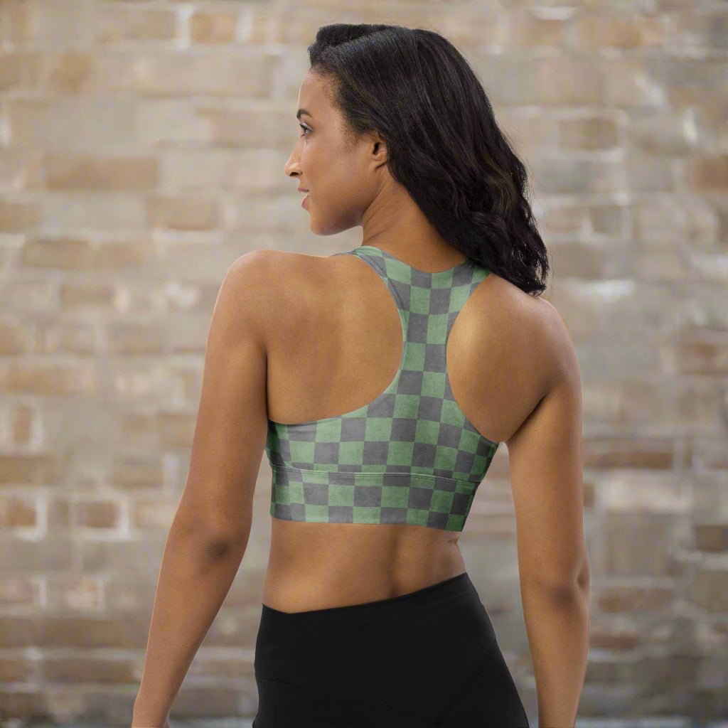 Woman wearing a green checkered sports bra and black leggings against a brick wall.