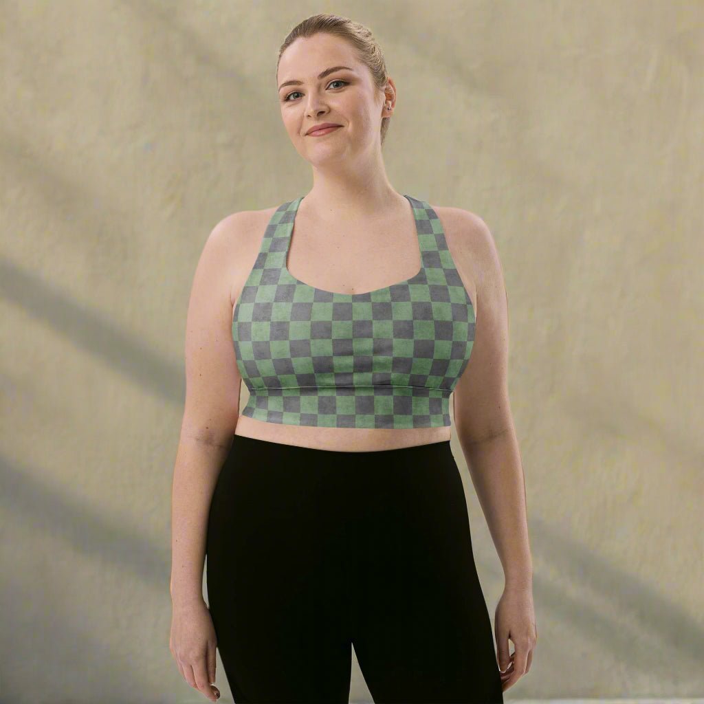 Woman wearing a green and gray checkered sports bra and black leggings on a neutral background
