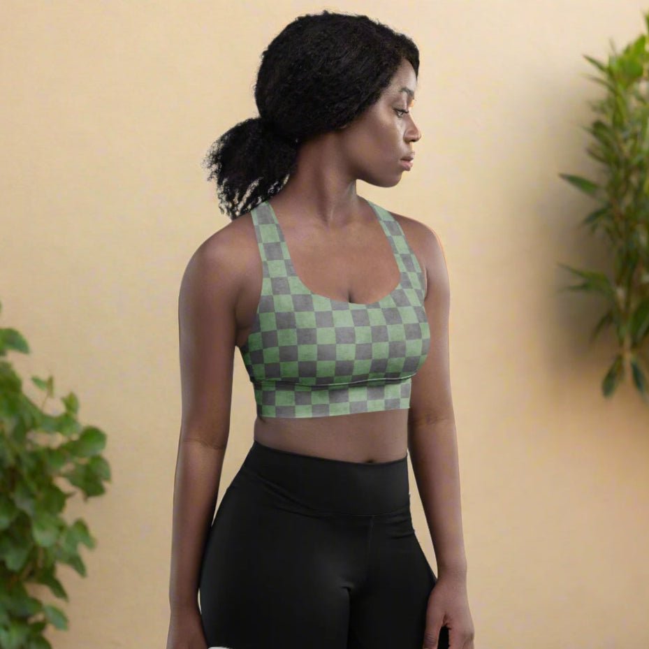 Woman wearing a green checkered sports bra and black shorts against a beige wall with plants.