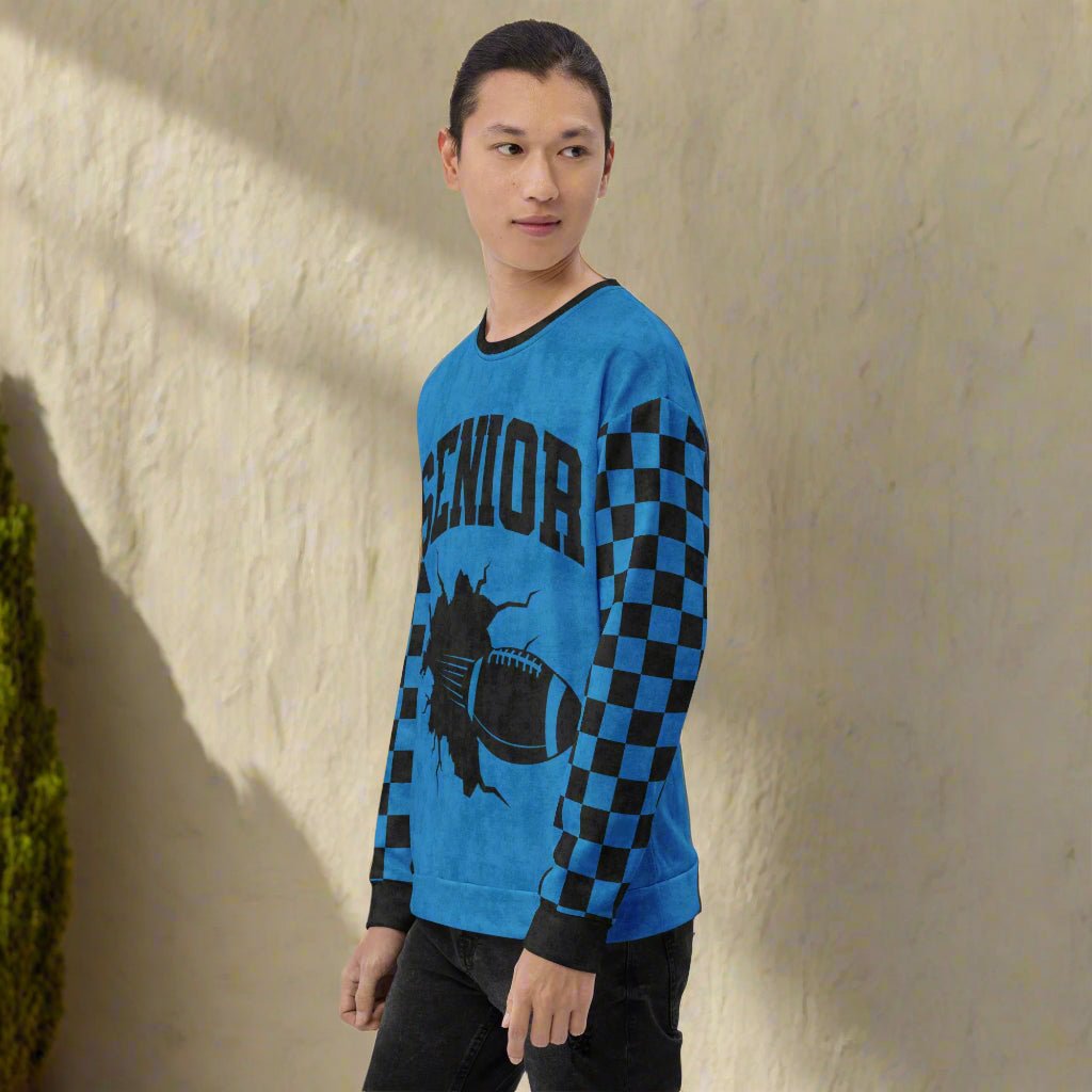 Person wearing a blue long-sleeve sweatshirt with checkered pattern and "Senior" football design against a beige wall.