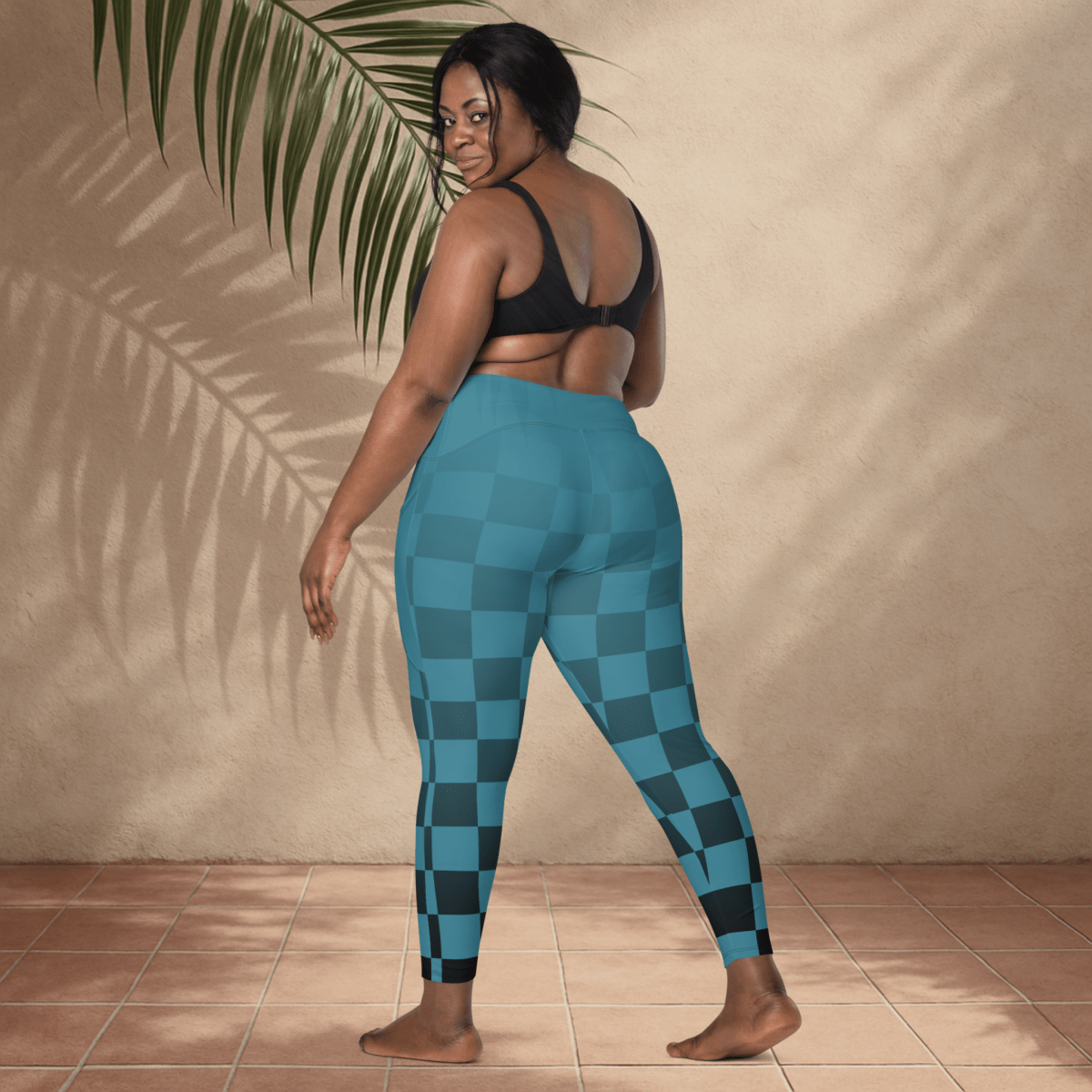 Person wearing blue checkered leggings standing against a beige wall with a plant.