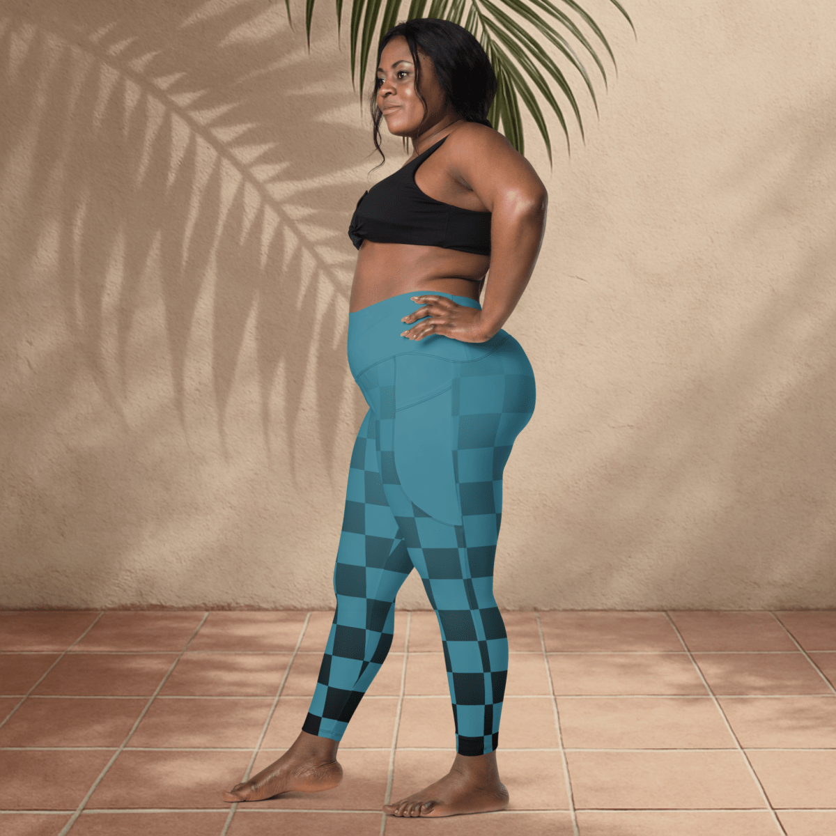 Woman wearing blue checkered leggings and black sports bra standing against a beige wall.