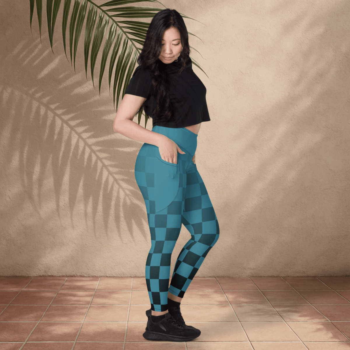 Woman wearing blue checkered leggings and black top against a beige wall.