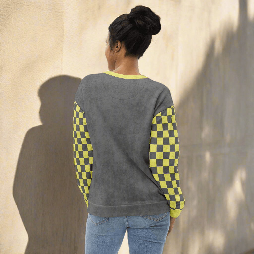 Person wearing a gray sweater with checkered sleeves against a textured wall.