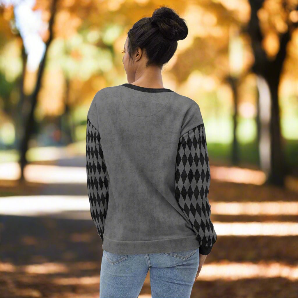 Person wearing a gray sweater with black diamond patterns in an autumn park.