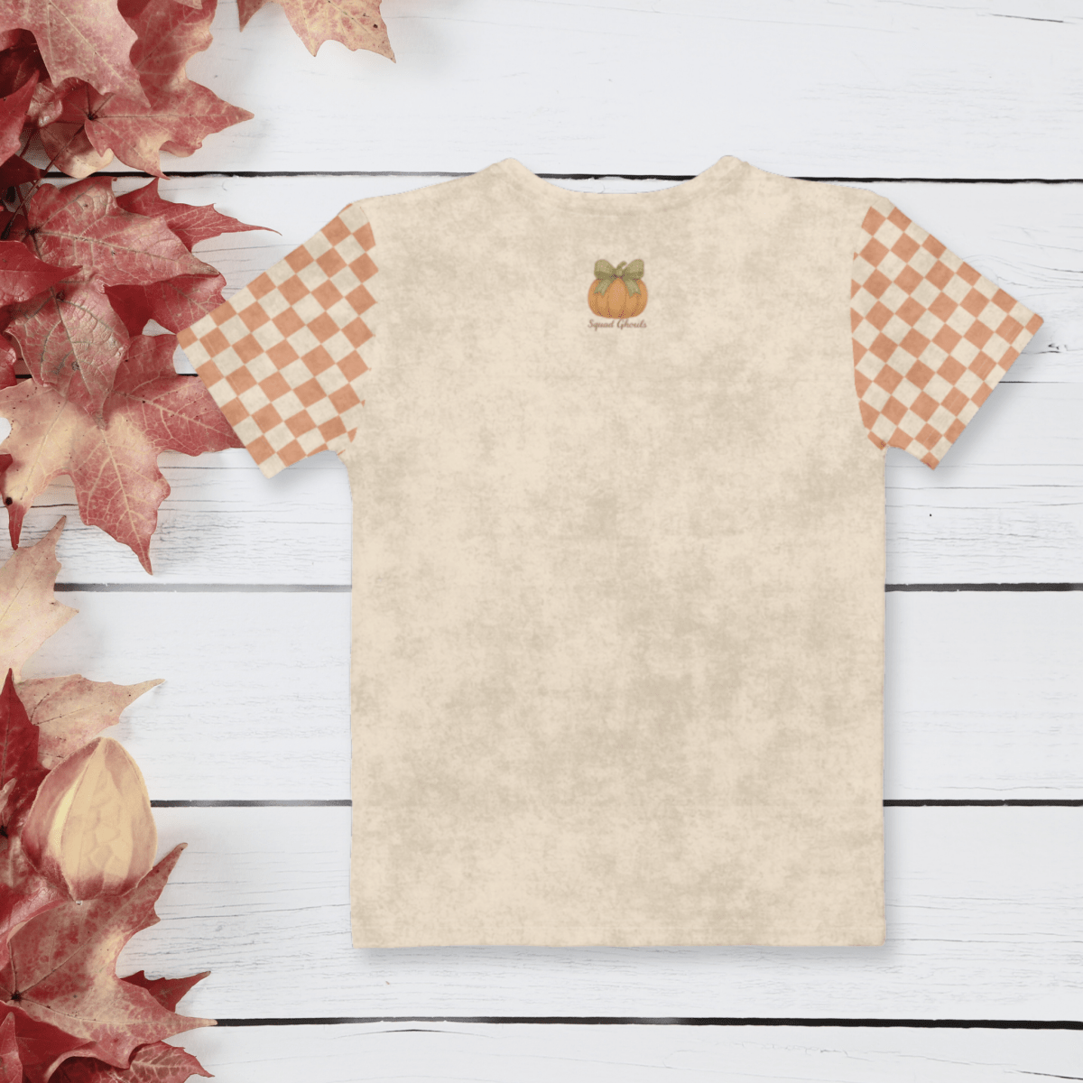 Beige t-shirt with checkered sleeves on a white wooden surface with autumn leaves.