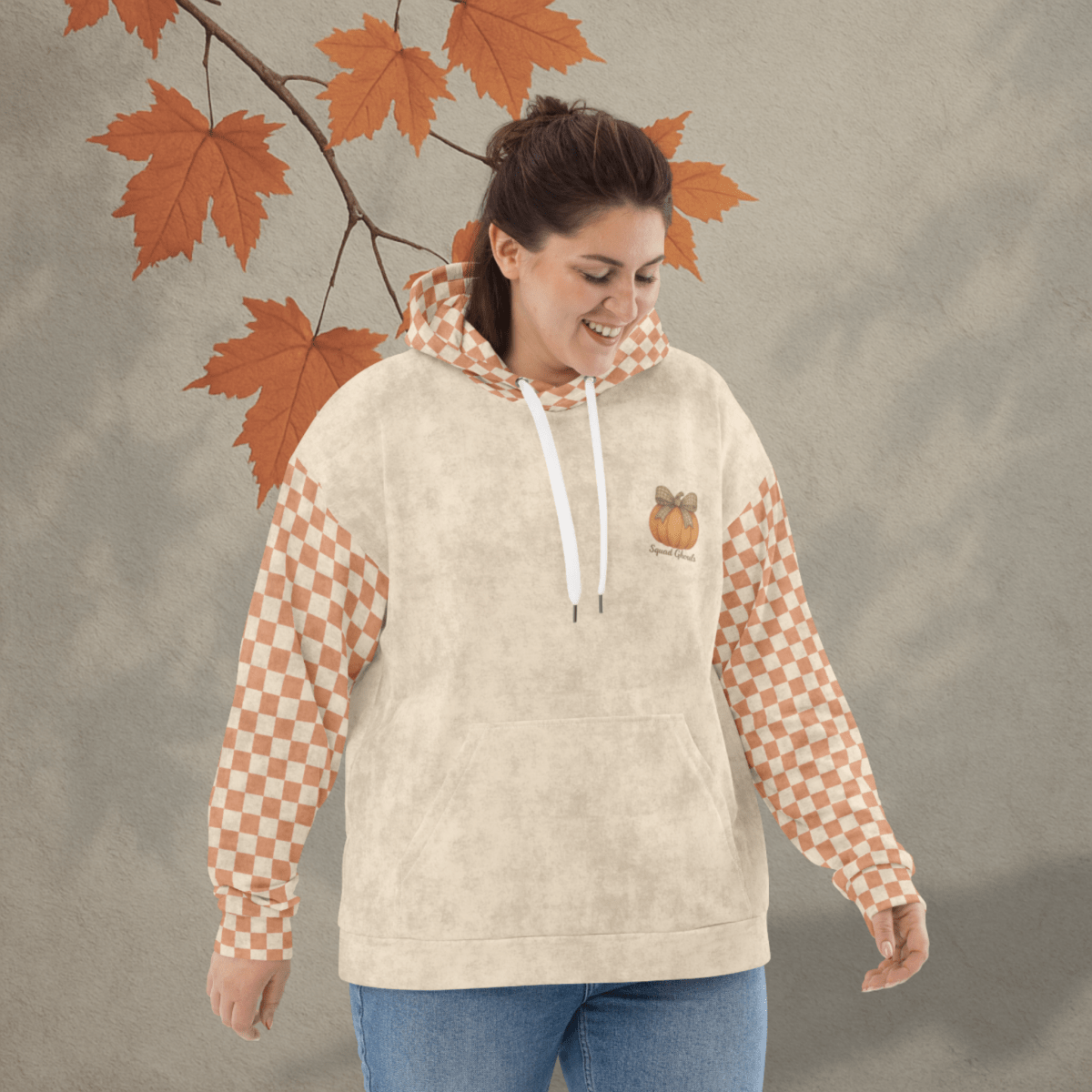 Woman wearing a beige hoodie with checkered sleeves against an autumn leaf background