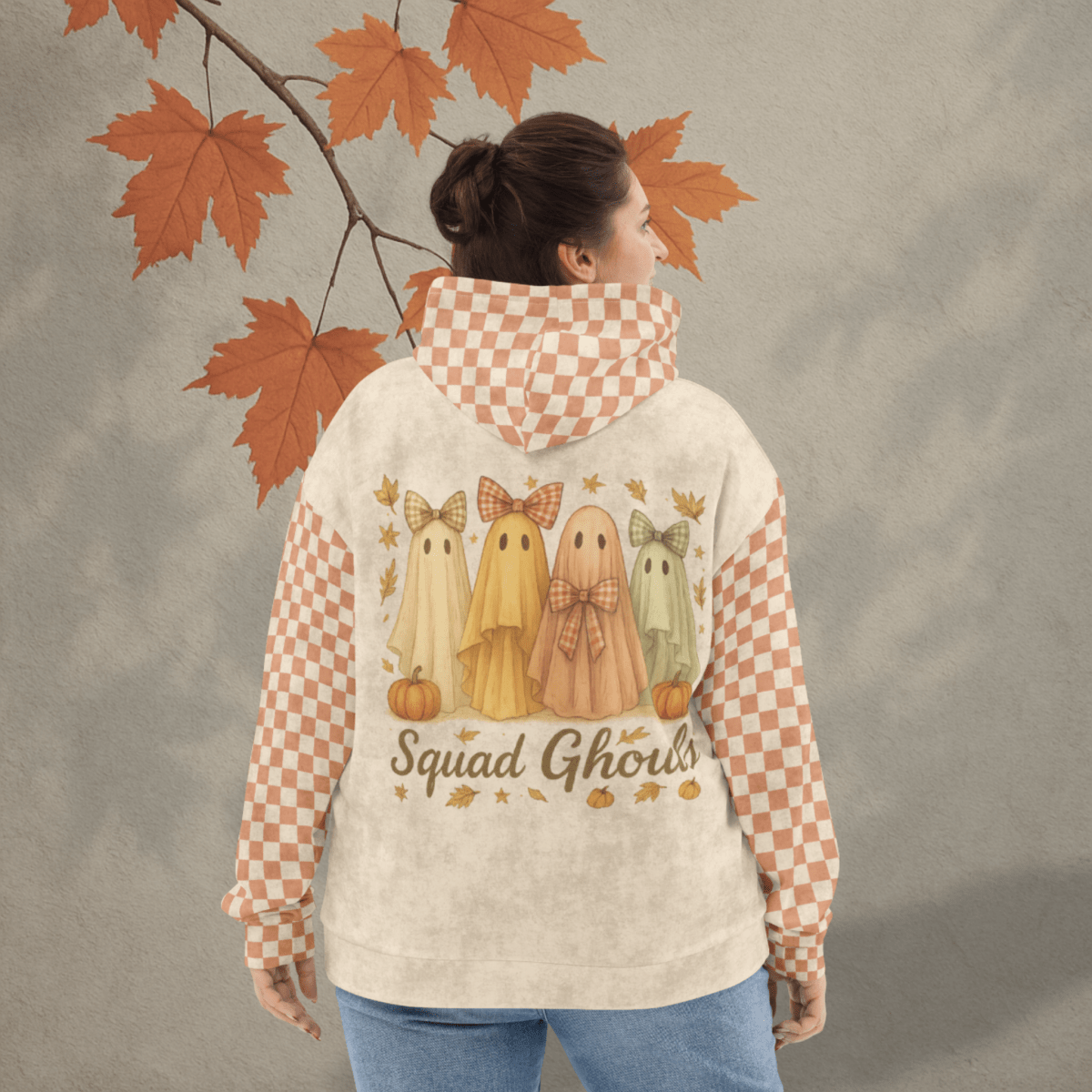 Person wearing a hoodie with ghost illustrations and 'Squad Ghouls' text, standing against a neutral background with autumn leaves.