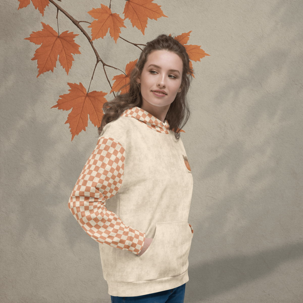 Woman wearing a beige hoodie with checkered sleeves against an autumn leaf background