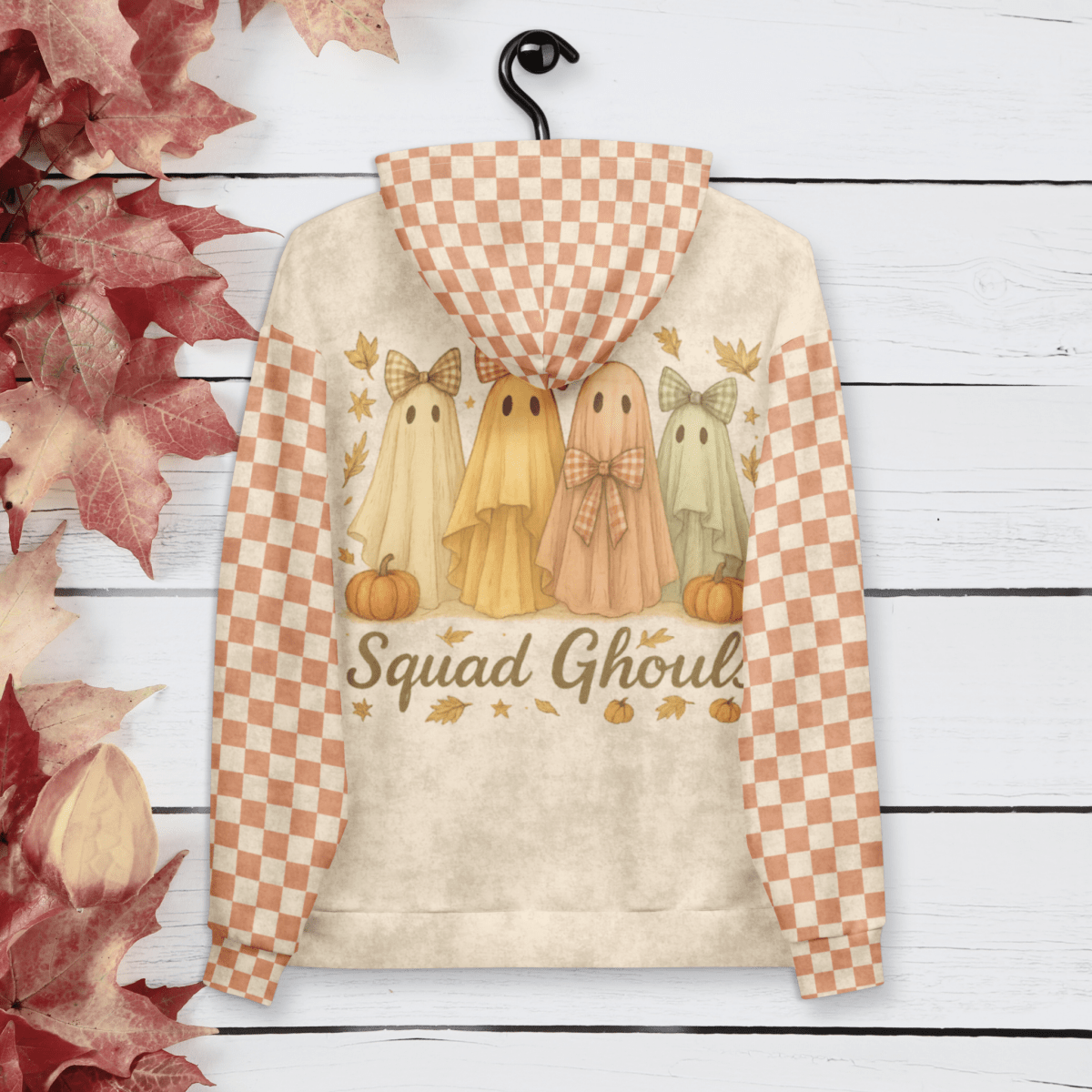 Hoodie with ghost design and 'Squad Ghouls' text on a wooden background with fall leaves.