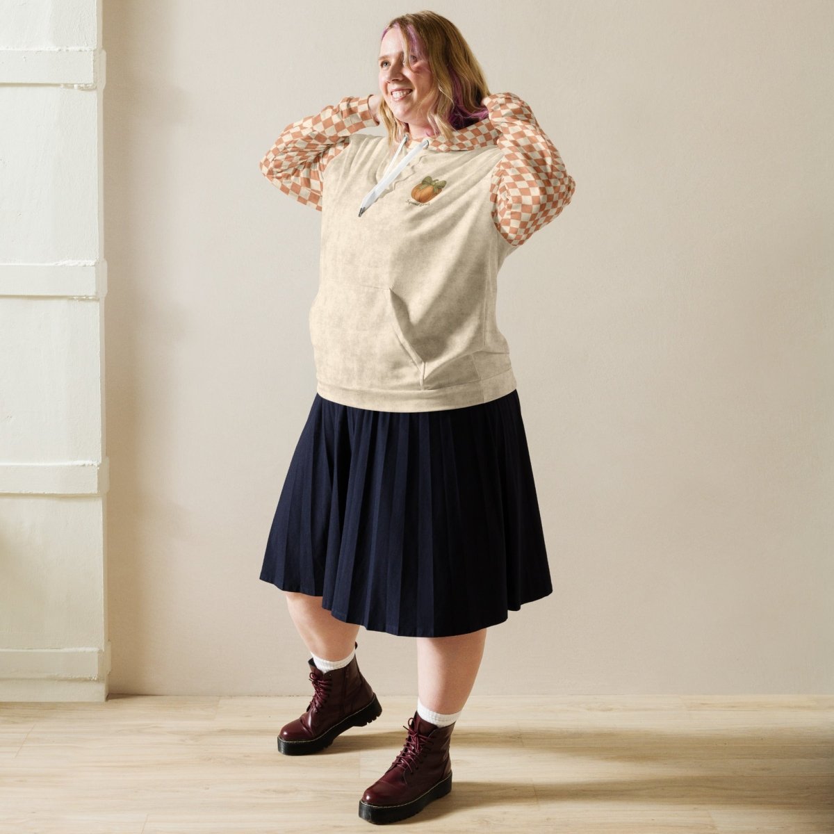 Person wearing a checkered sleeve hoodie, navy skirt, and dark shoes in a room with light-colored walls.