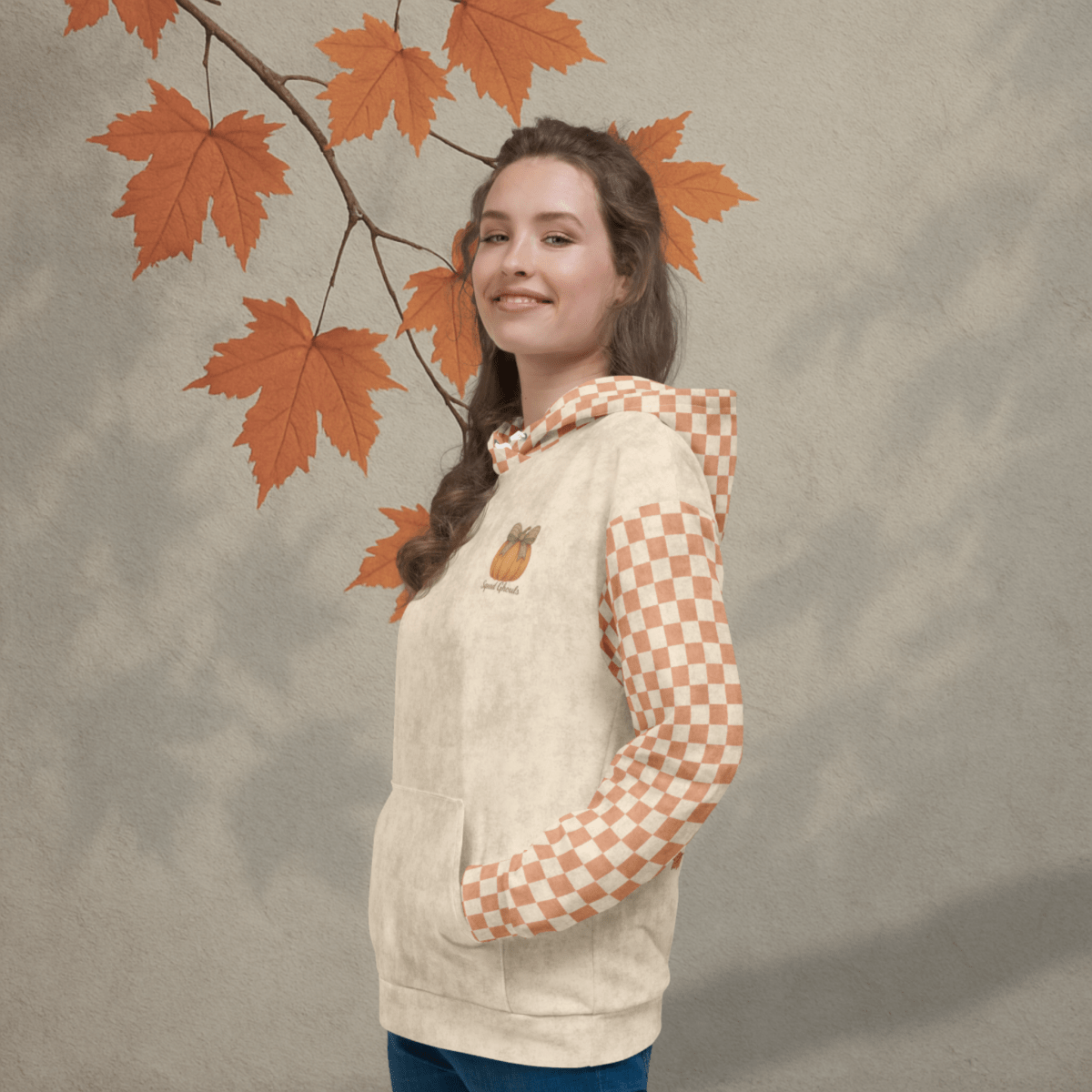 Woman wearing a beige hoodie with checkered sleeves against an autumn leaf background