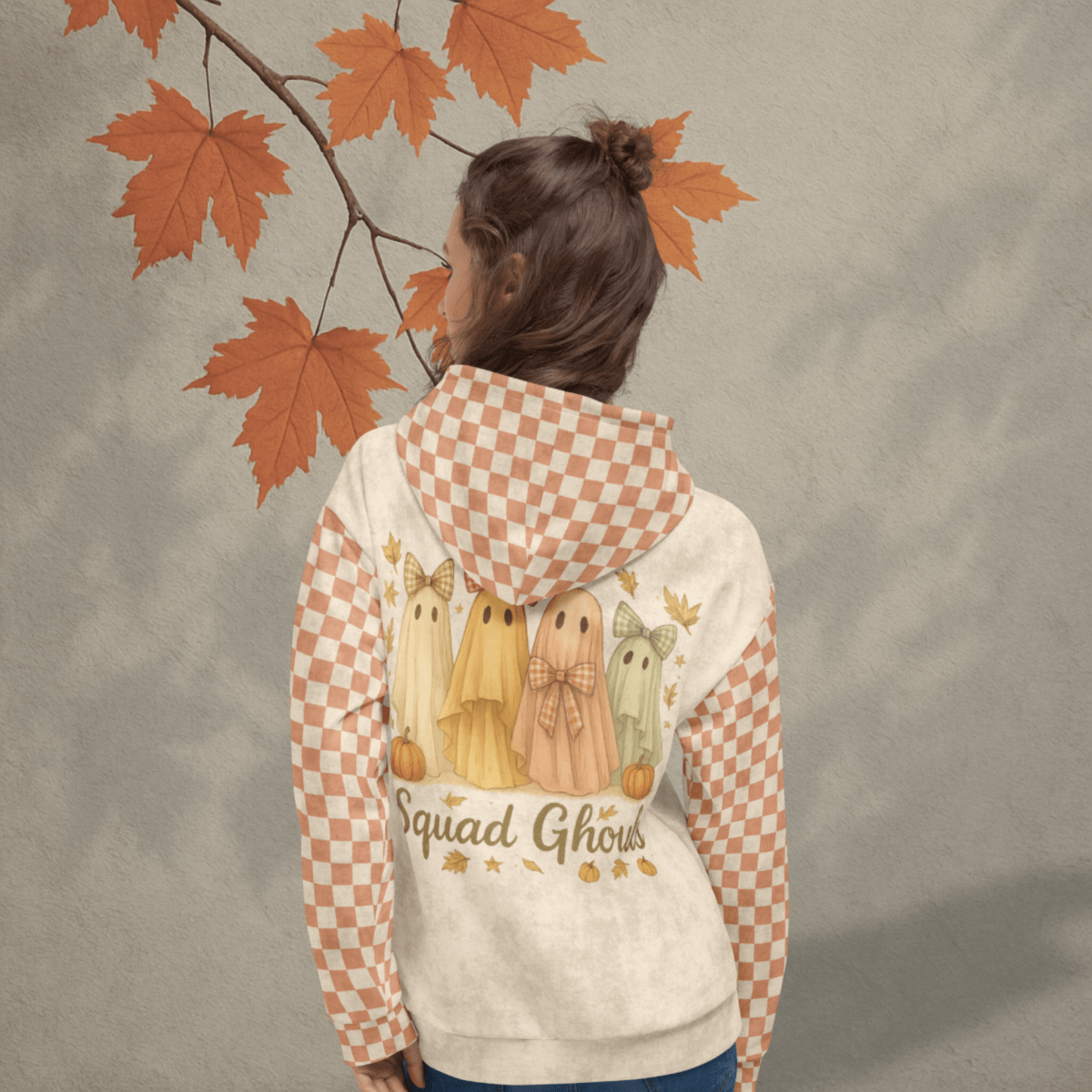 Person wearing a hoodie with ghost and pumpkin design, standing against a leafy background.