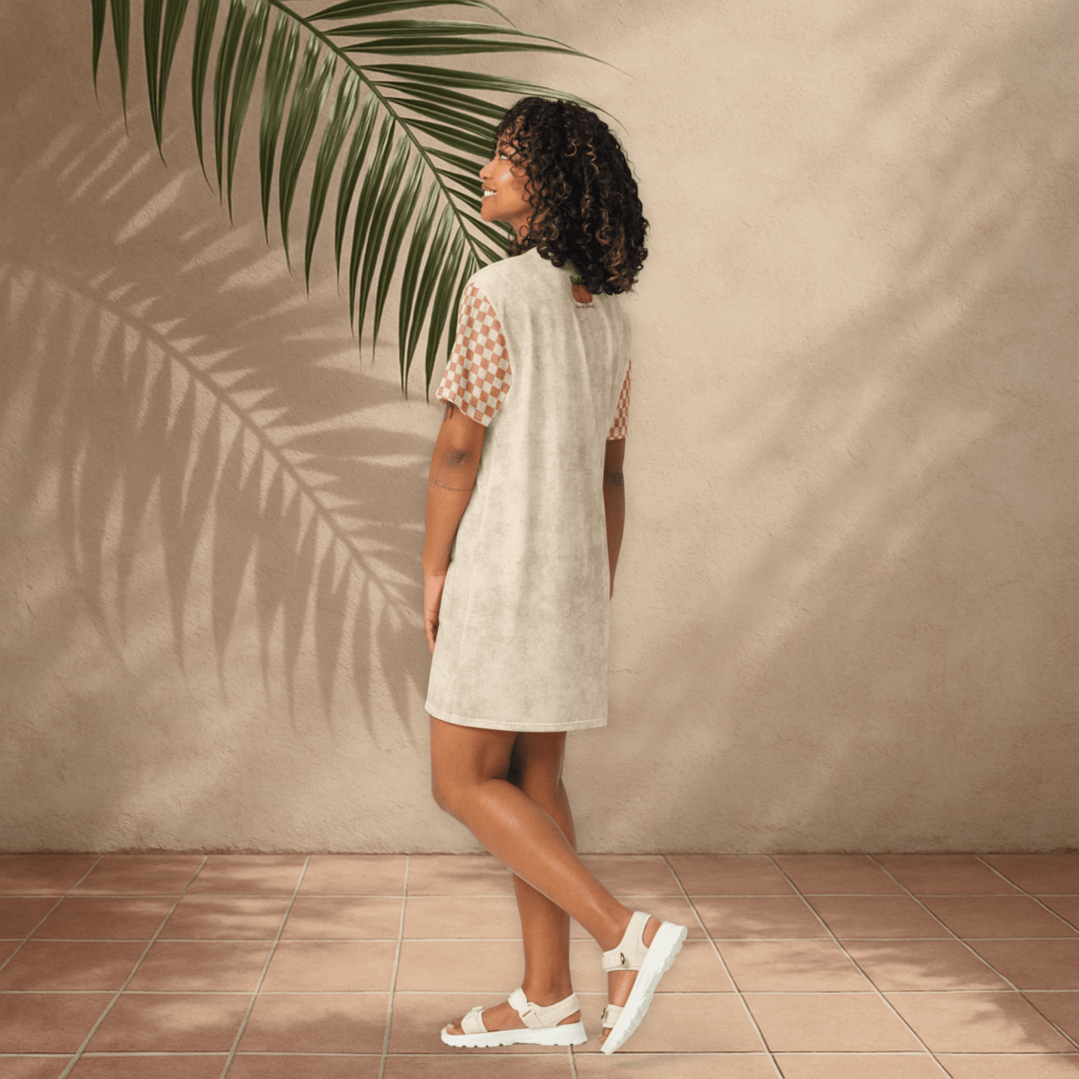 Woman in a light dress standing against a beige wall with a palm leaf