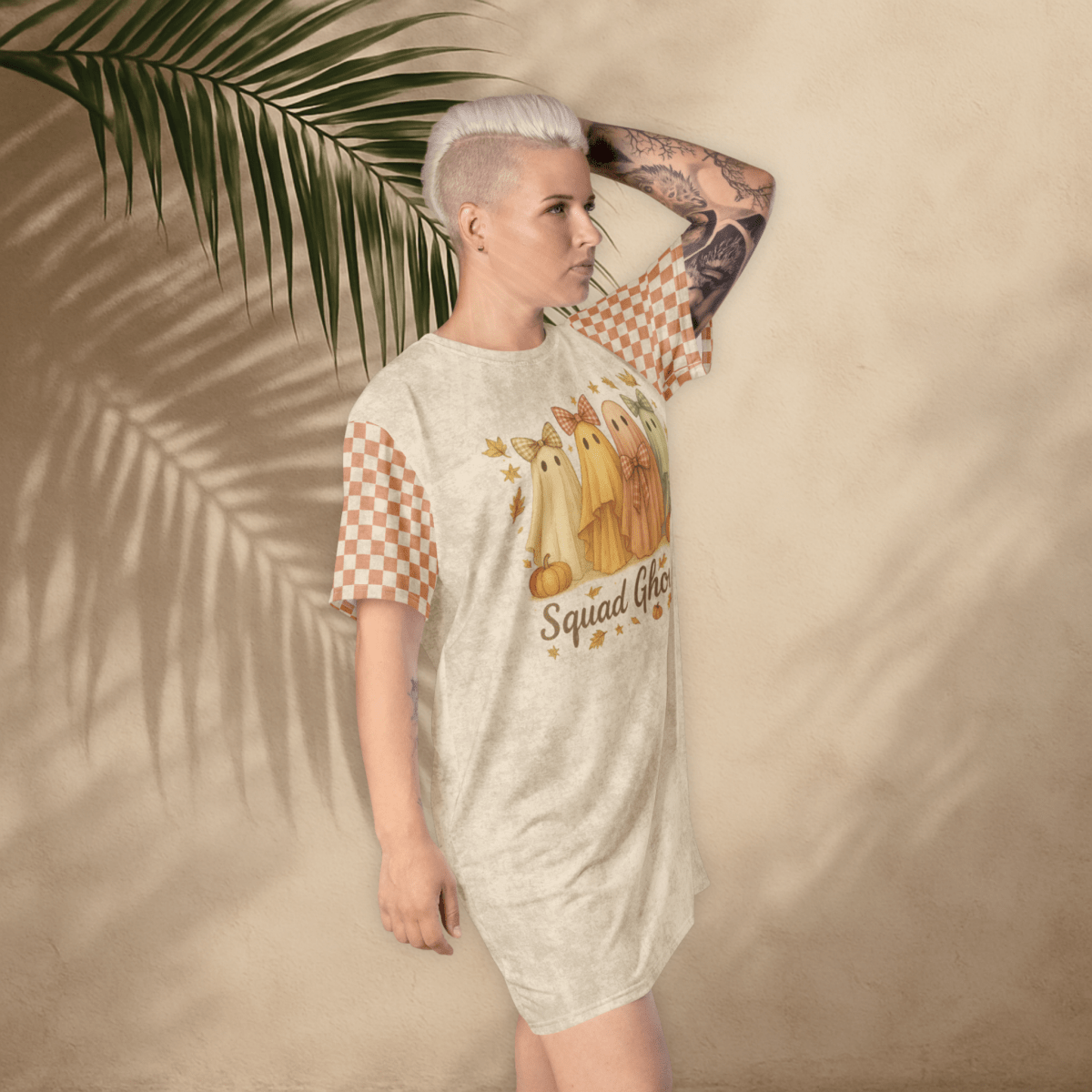 Person wearing a t-shirt dress with a ghost design and text, standing against a beige wall with a palm leaf.