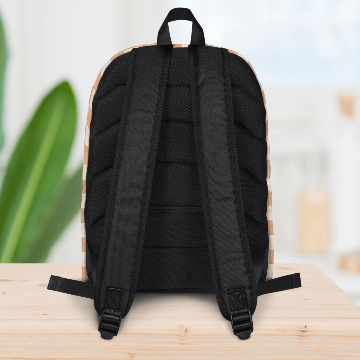 Backside of a backpack on a wooden surface with a blurred plant and light background