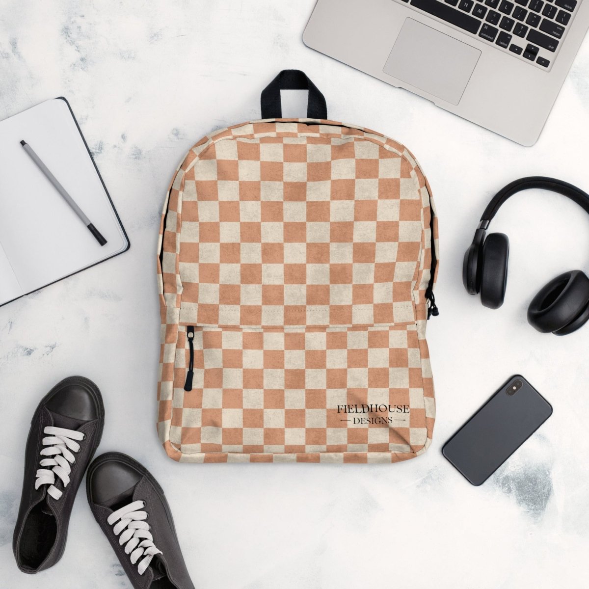 Checkered backpack on a marble surface with a laptop, headphones, phone, and shoes.