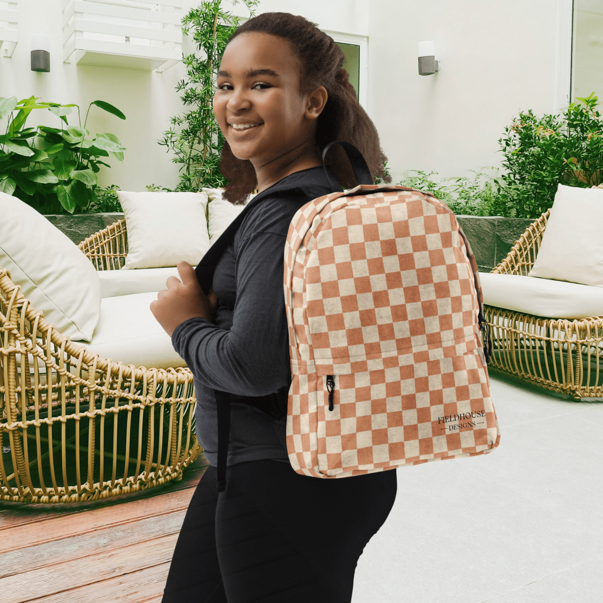 Person wearing a checkered backpack in an outdoor setting with furniture and plants.