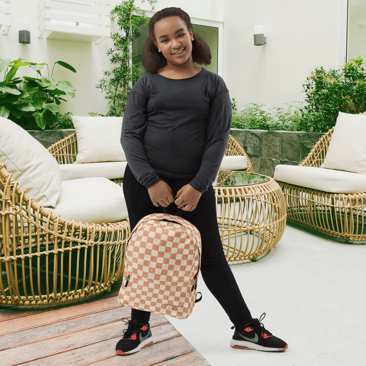 Person holding a checkered backpack in an outdoor setting with wicker furniture and plants.