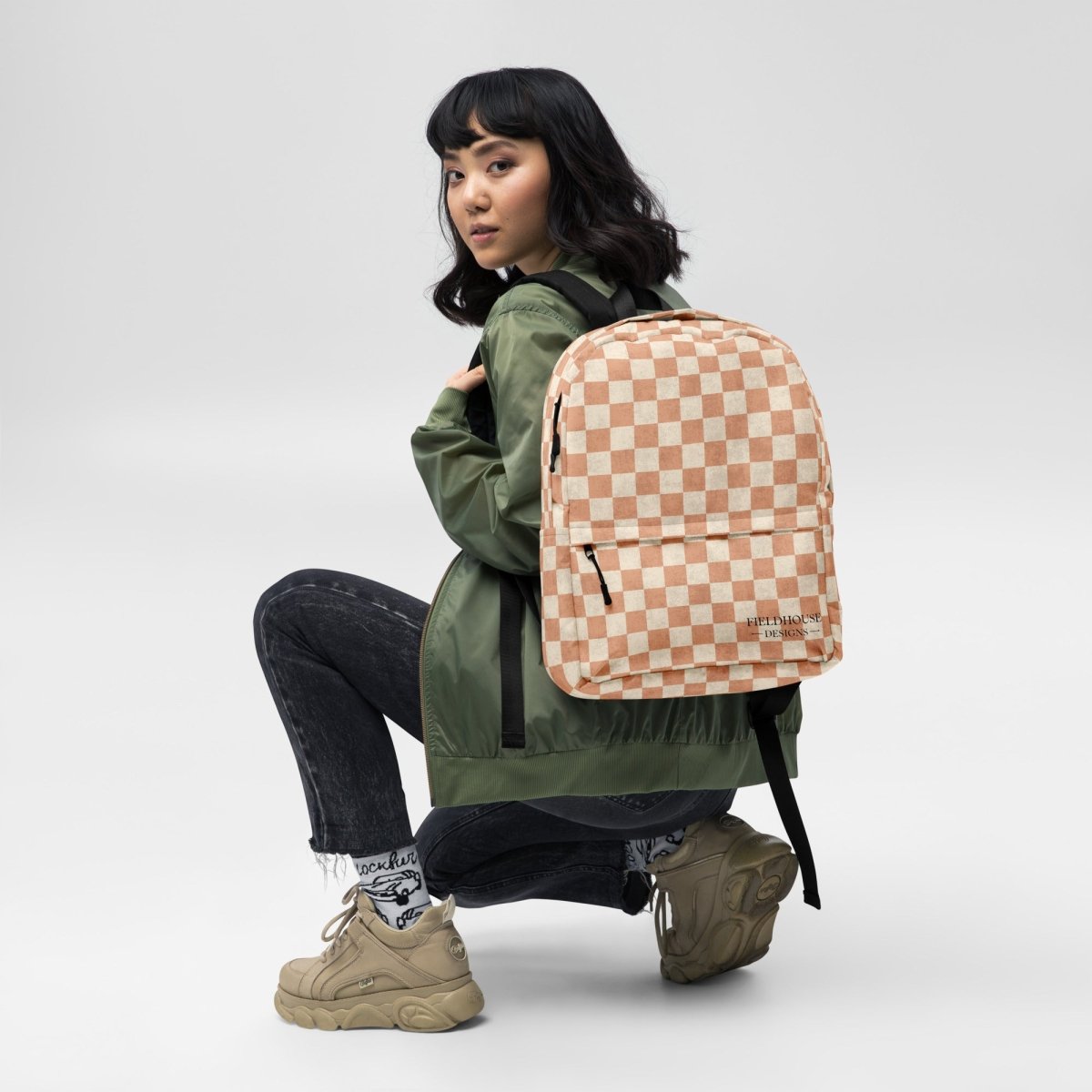 Person wearing a green jacket with a checkered backpack on a white background