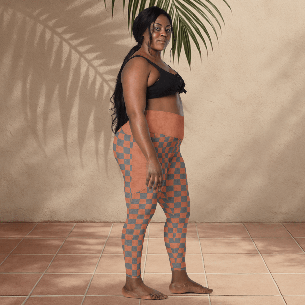 Woman wearing checkered leggings standing against a beige wall with a plant.