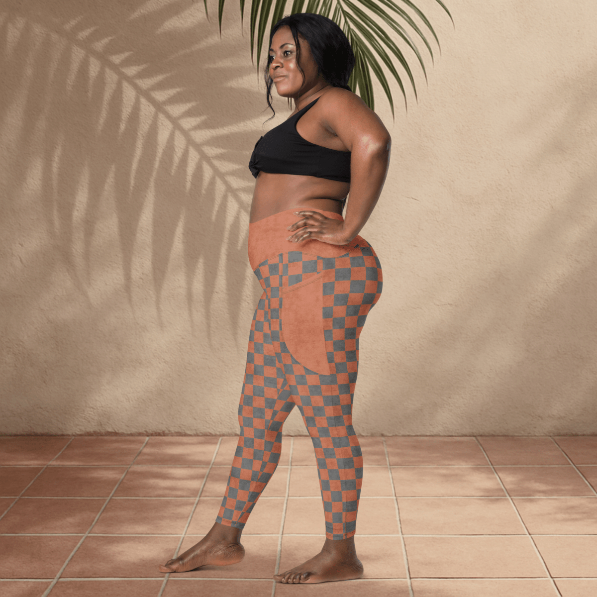 Woman wearing checkered leggings and black sports bra against a beige wall.