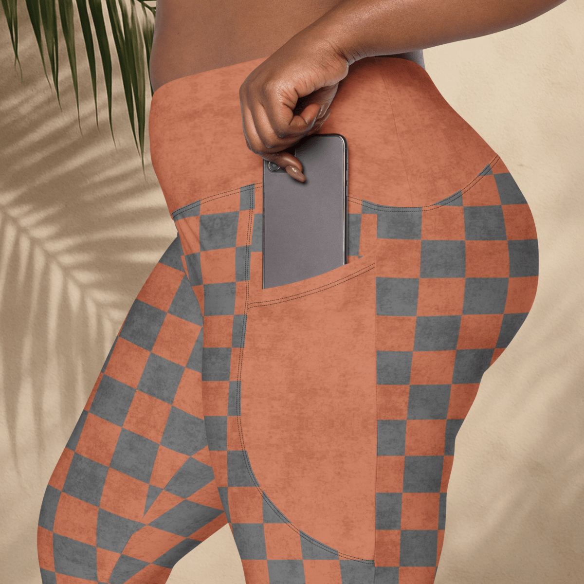 Person wearing checkered pants with a pocket holding a phone, against a neutral background.