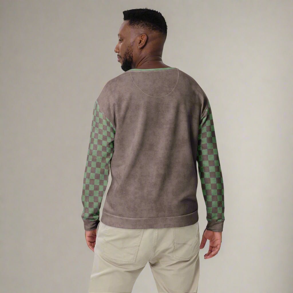 Man wearing a brown sweater with green checkered sleeves on a neutral background