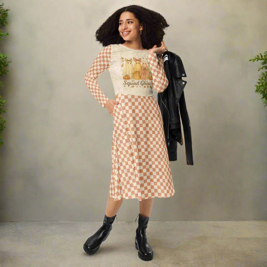 Woman wearing a checkered dress with a graphic top, holding a black jacket against a neutral background