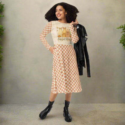 Woman wearing a checkered dress with a graphic top, holding a black jacket against a neutral background