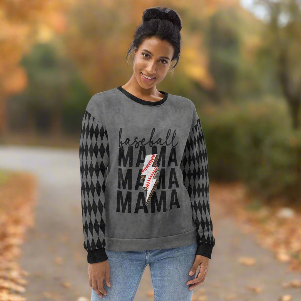 Woman wearing a gray sweater with 'baseball MAMA' text, standing outdoors with blurred foliage in the background.
