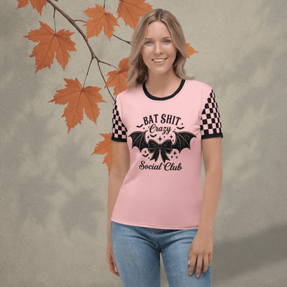 Person wearing a pink t-shirt with black text and checkered sleeves, standing against a neutral background with autumn leaves.