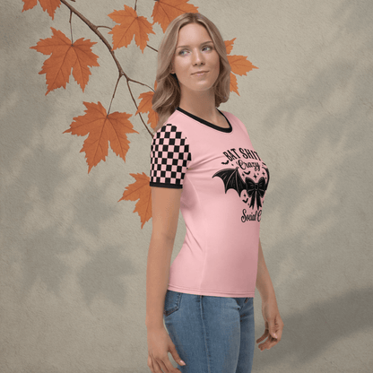 Woman wearing a pink t-shirt with a black checkered sleeve and graphic design, standing against a textured wall with orange leaves.