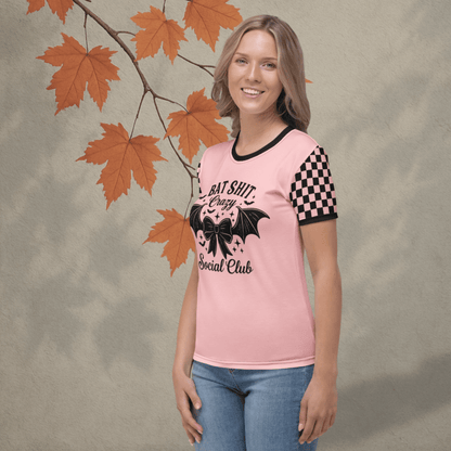 Woman wearing a pink t-shirt with black text and graphics, standing against a neutral background with autumn leaves.