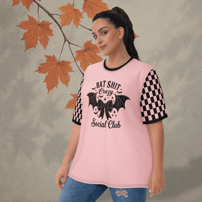Woman wearing a pink t-shirt with black text and graphics, standing against a neutral background with autumn leaves.