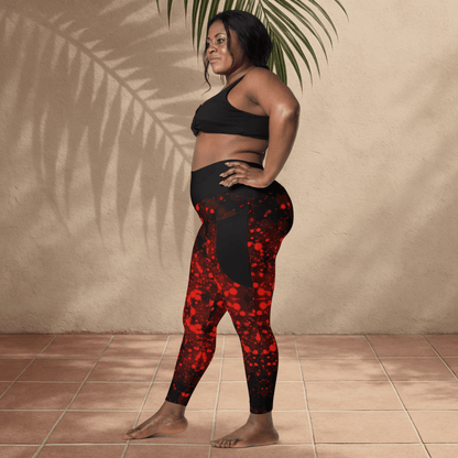 Woman wearing black sports bra and black with red patterned leggings standing against a beige wall.