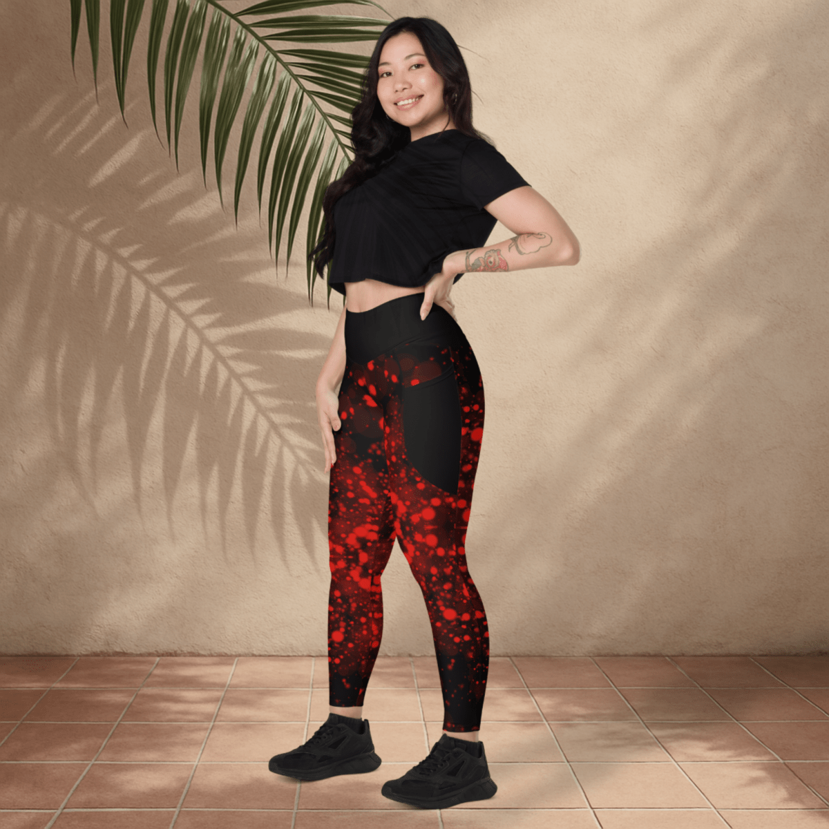 Woman wearing black and red patterned leggings with a black crop top against a beige wall.