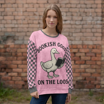 Person wearing a pink sweater with a goose graphic and text in front of a brick wall