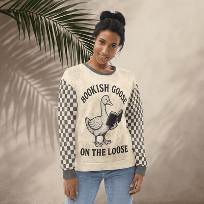 Woman wearing a sweater with a goose graphic and text, standing against a beige wall with a leafy branch.