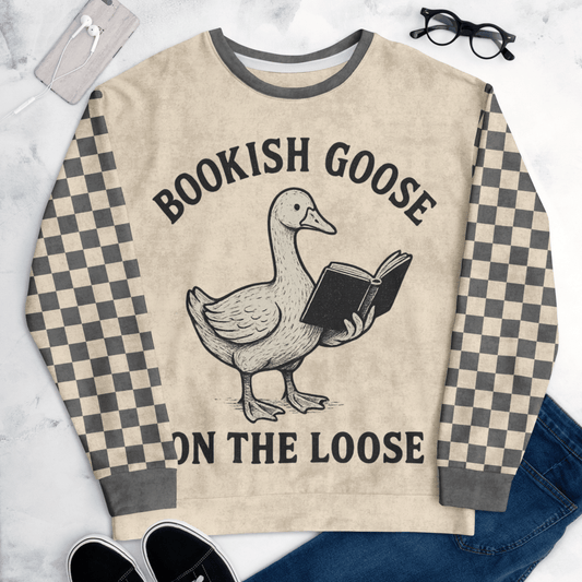 Beige sweater with a goose holding a book and text 'Bookish Goose on the Loose' on a marble surface.
