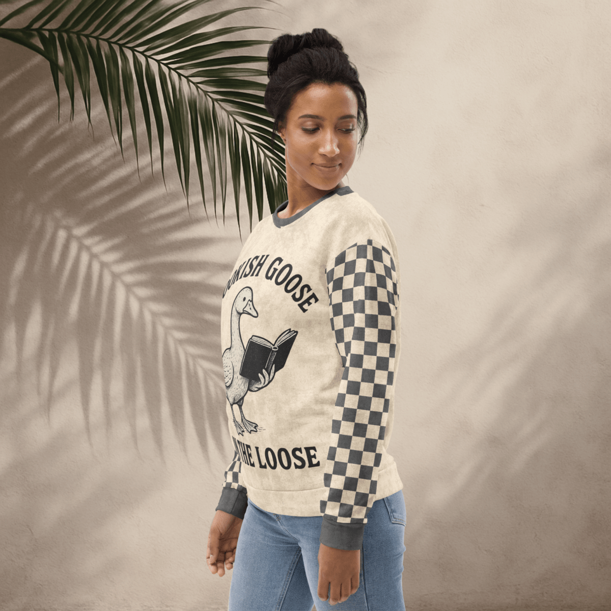 Woman wearing a sweater with a graphic design and text, standing against a neutral background with a palm leaf.