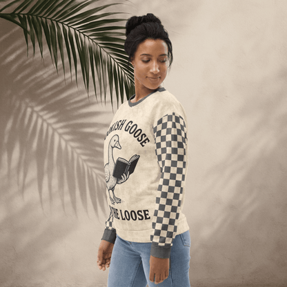 Woman wearing a sweater with a graphic design and text, standing against a neutral background with a palm leaf.