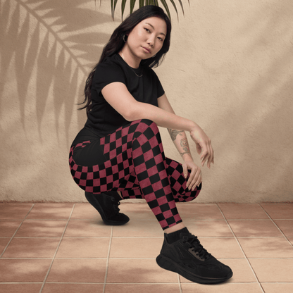 Person wearing a black t-shirt and burgundy checkered pants sitting on the floor with a leaf above them against a beige wall.