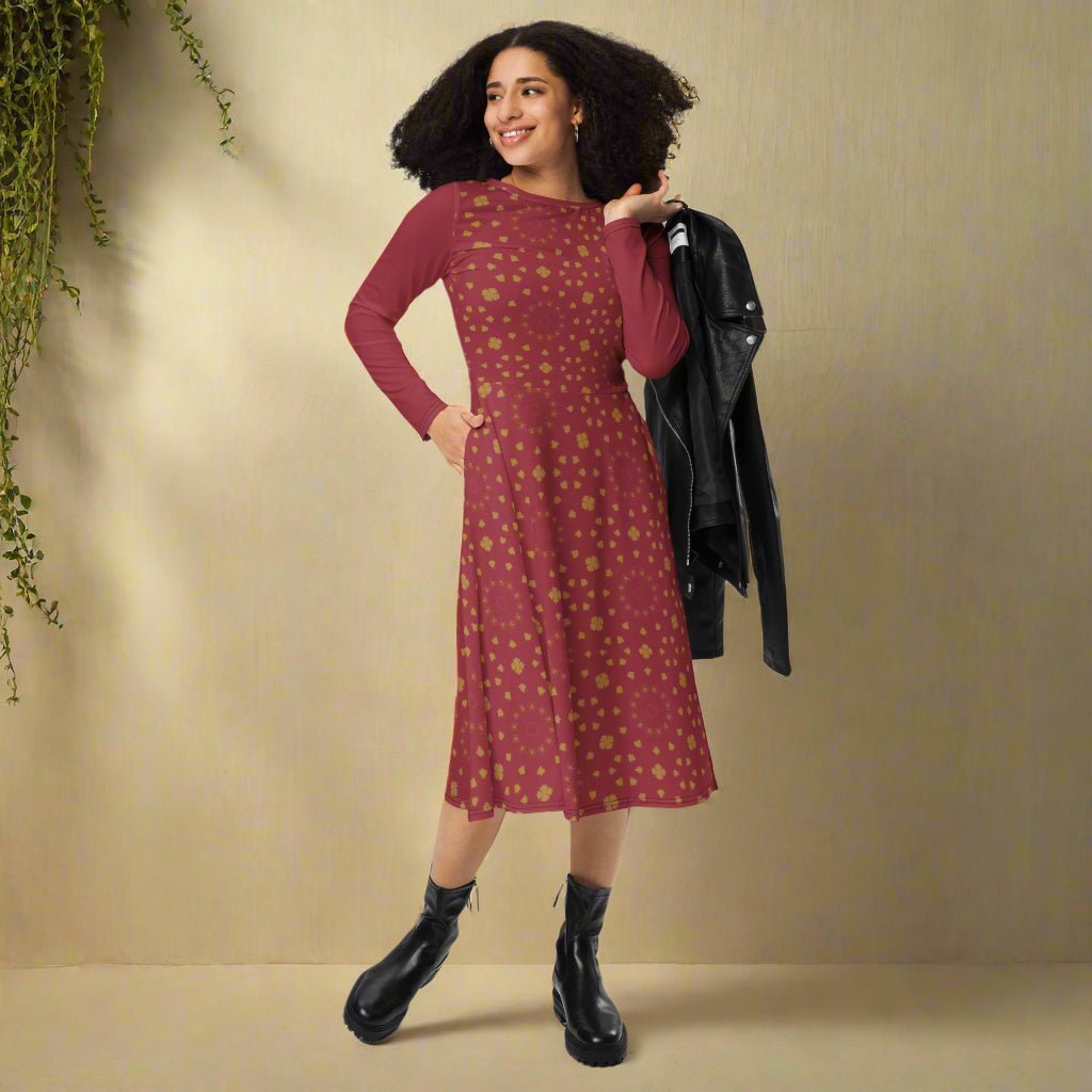 Woman wearing a burgundy boho patterned dress holding a black jacket against a beige wall.