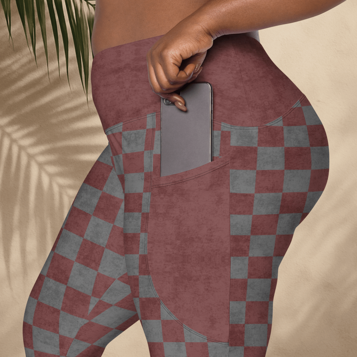 Person wearing burgundy and gray checkered leggings with a pocket, holding a phone.