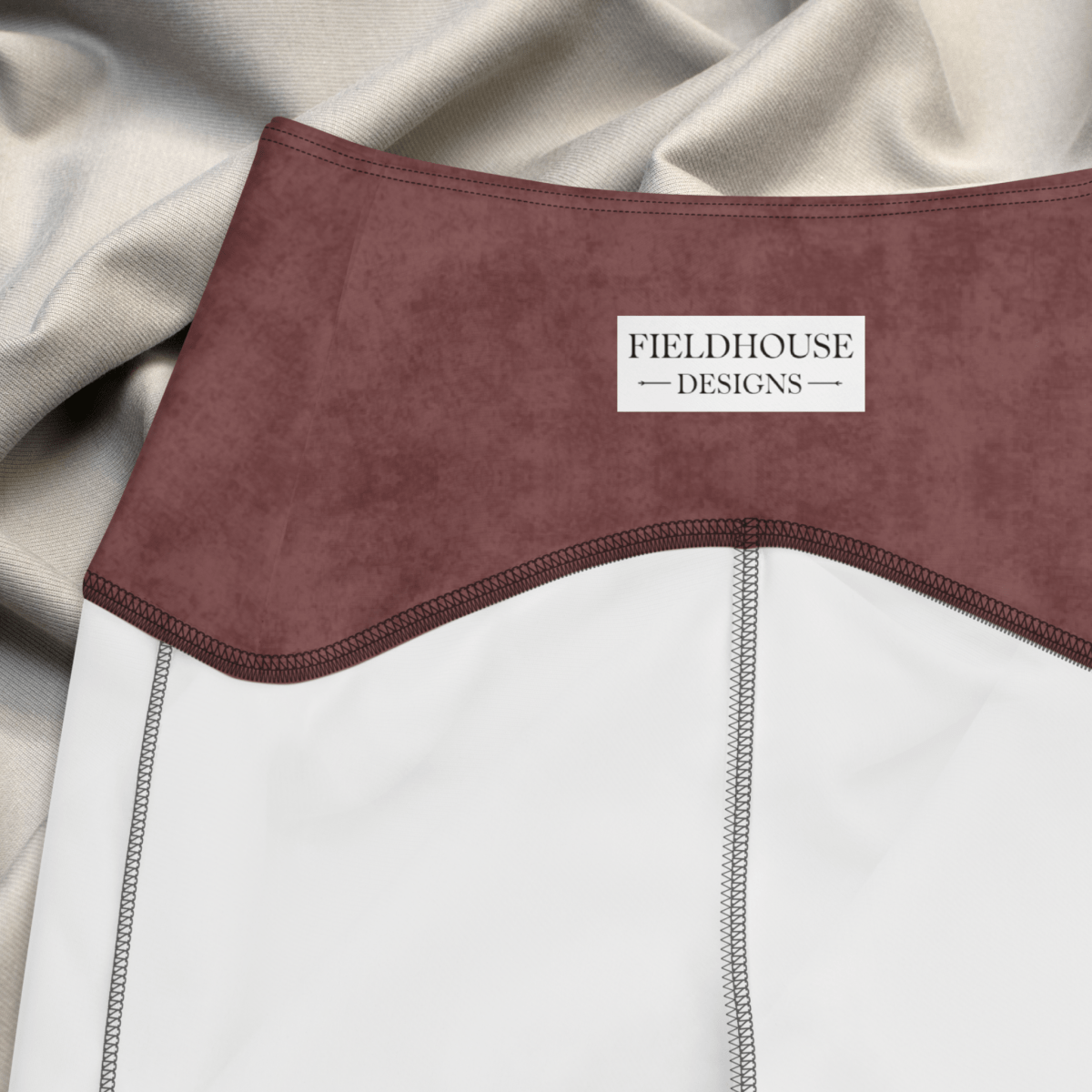 Close-up of a garment with a burgundy waistband and 'Fieldhouse Designs' label on a beige fabric background.