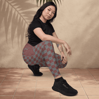 Person wearing a black t-shirt and checkered pants sitting on the floor with a leaf above them against a beige wall.