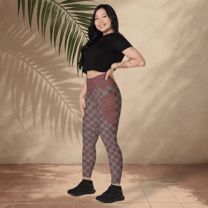 Woman wearing checkered leggings and a black top standing against a beige wall with a plant.