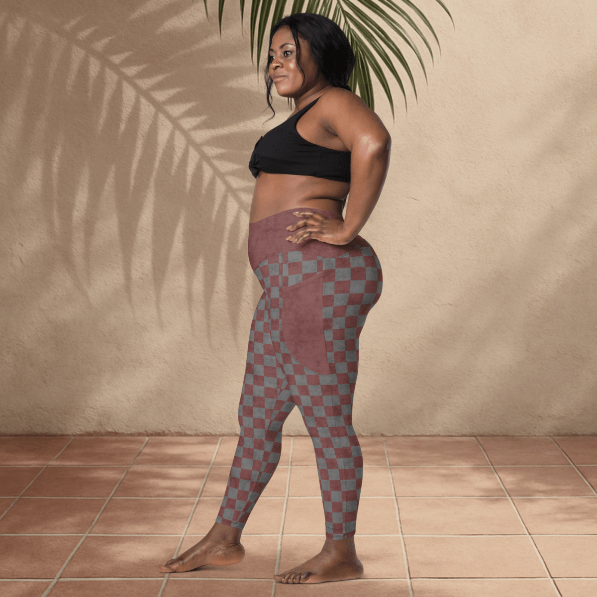 Woman wearing checkered leggings and black sports bra against a beige wall.
